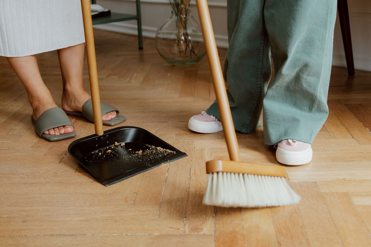 services-01 Close-up of people cleaning wooden floor with broom and dustpan indoors.